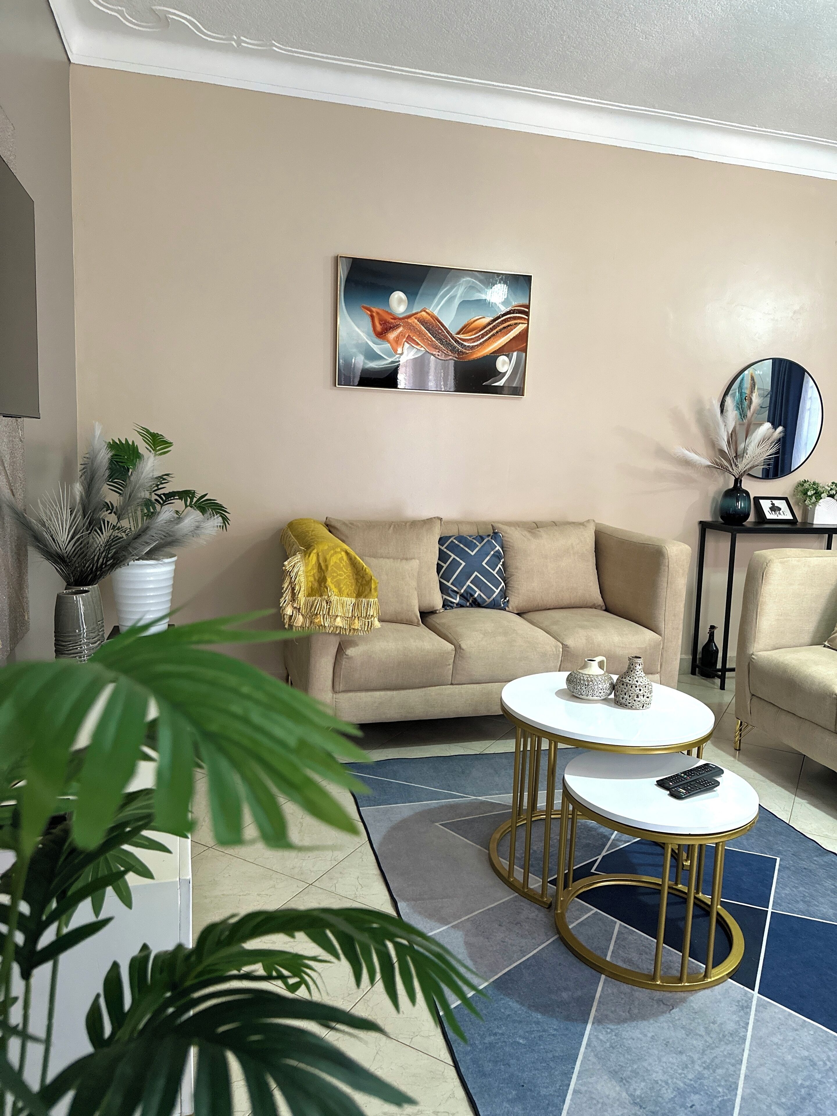 Una sala de estar con un sofá color beige, dos mesas blancas para café y un cuadro abstracto grande en la pared.