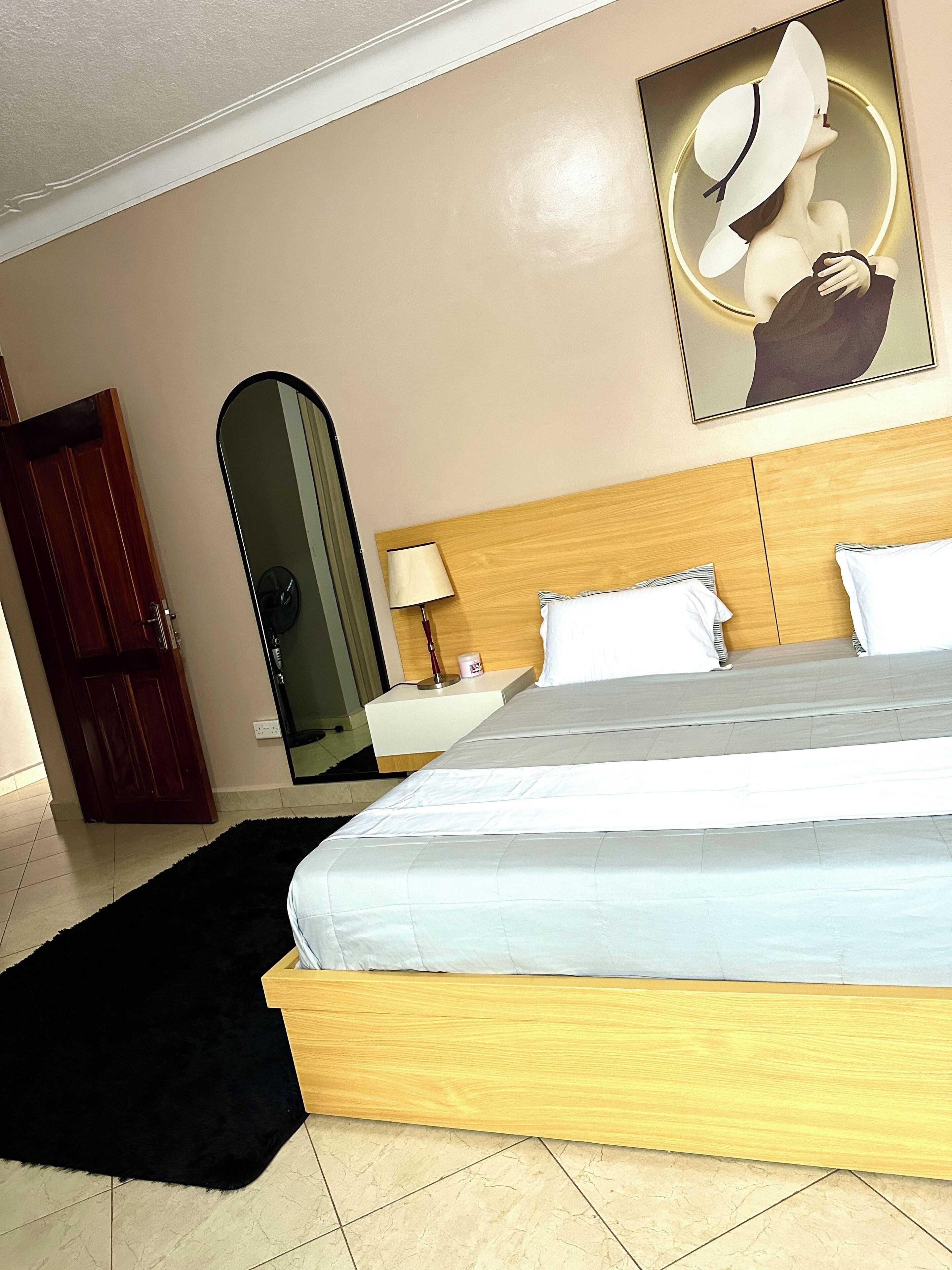 A hotel room with a bed, a nightstand, a lamp, a mirror, and a door.