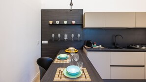 A modern kitchen with dark cabinetry, a black countertop, and a dining area with a table set for four. - Bisicool Boutique Apartment by Napoliapartments (Naples)