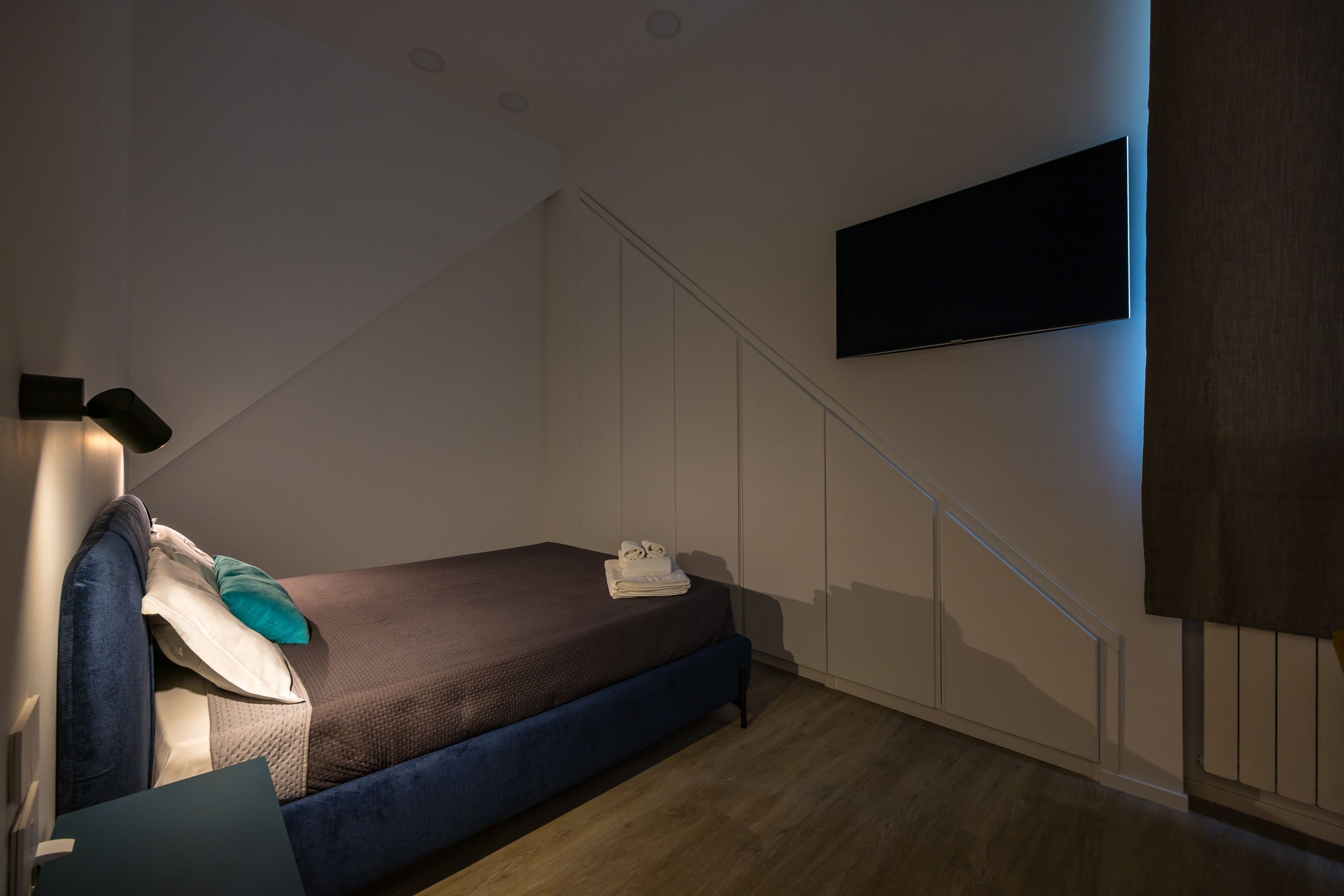 A bedroom with a bed, a TV mounted on the wall, and a staircase.