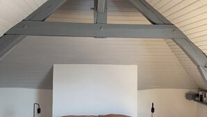Ein Schlafzimmer mit schrägem Dach, einem Bett mit rosa Bettwäsche und zwei Nachttischlampen.