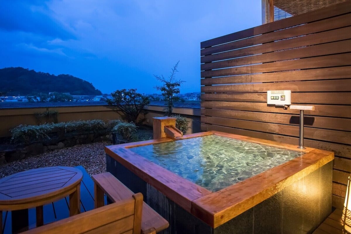 Een hottub met houten zitplaatsen en een lantaarn, geplaatst tegen een houten muur met uitzicht op een verafgelegen landschap.
