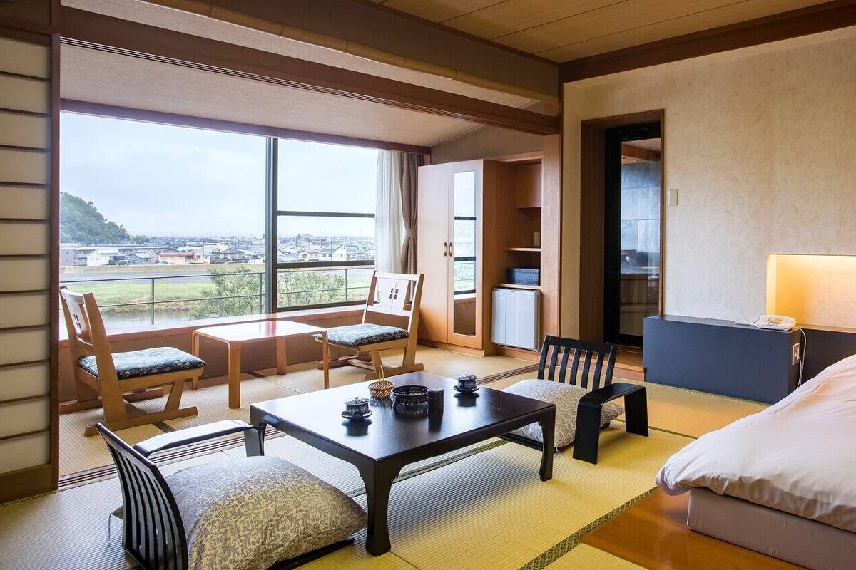 Een hotelkamer met tatami vloeren, een lage tafel met theeserviesjes, een bank, een bed en uitzicht op de stad.