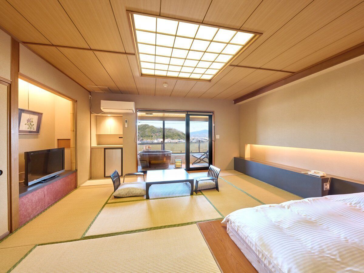 Hotelkamer met tatami matten, een bed, een televisie, een jacuzzi en uitzicht op een berg.