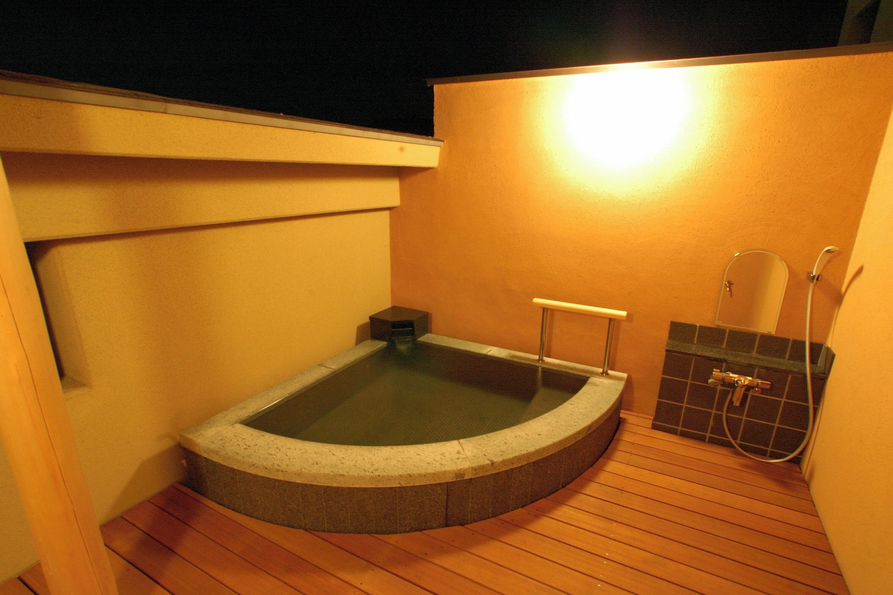 Een hottub op een houten terras, met een betegelde muur en een douchegedeelte.