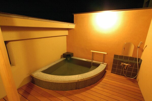 Un jacuzzi en una terraza de madera con un muro de azulejos y zona de ducha.