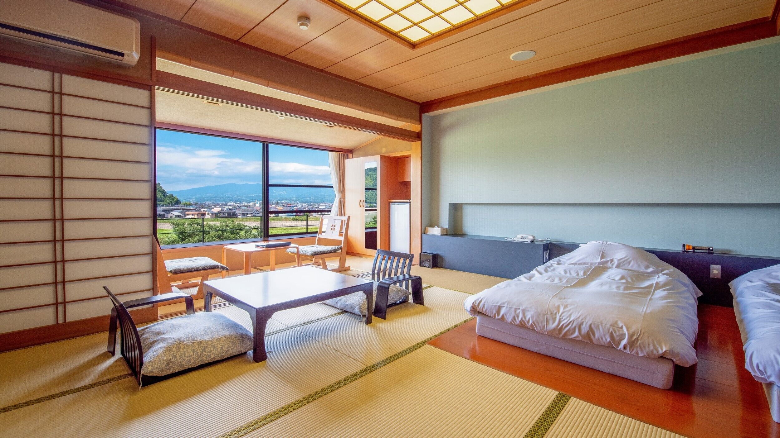 Une chambre d’hôtel avec un sol recouvert de tatamis, un lit, un bureau et une vue sur la ville.