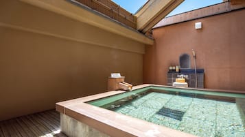 Un área de hidromasaje con terraza de madera, pared de piedra y un estante con botellas.