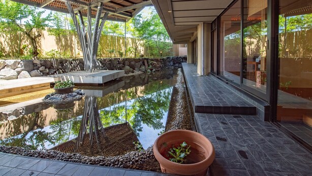 A modern building with a covered outdoor area, a reflective water feature, and a stone wall.