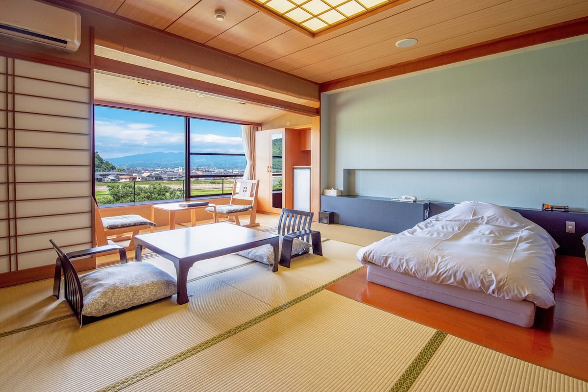 Een moderne hotelkamer met tatami vloeren, een groot bed, een bureau en uitzicht op een stadsgezicht.