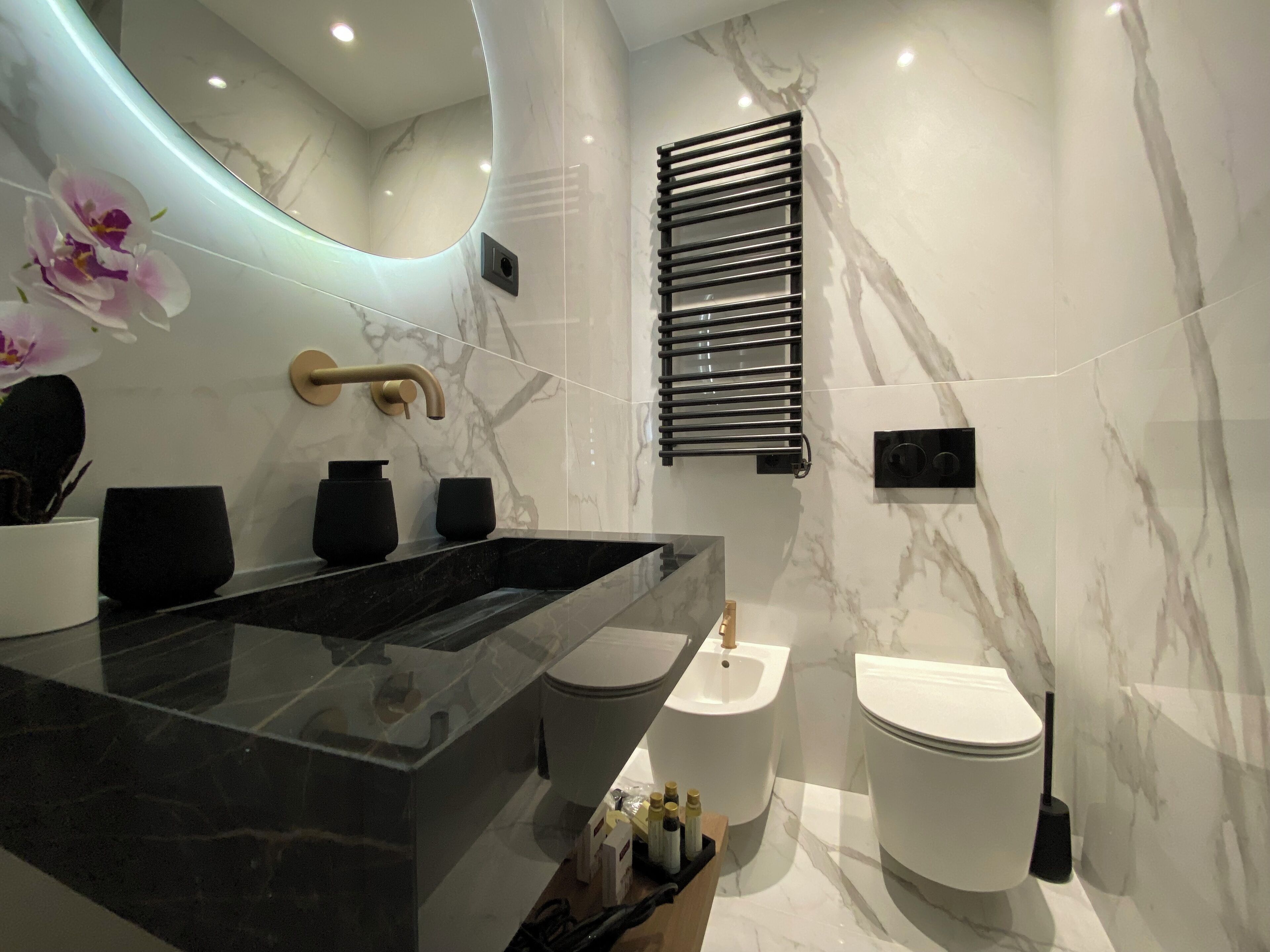 A modern bathroom with a marble vanity, a black sink, a gold faucet, a black towel rack, and a white toilet.