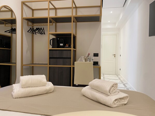 A modern bedroom with a large bed, a wardrobe with multiple shelves, a mirror, and a bedside table with a lamp. - Suite Croce (Rome)