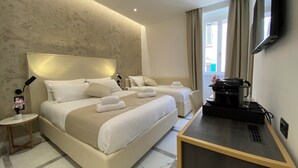 Habitación de hotel con una cama grande, una cama más pequeña, un escritorio con cafetera y un televisor en la pared.