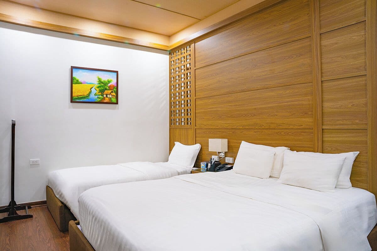 Ein Hotelzimmer mit zwei Betten, einem Holzkopfstück, einem Gemälde an der Wand und einer Stehlampe.