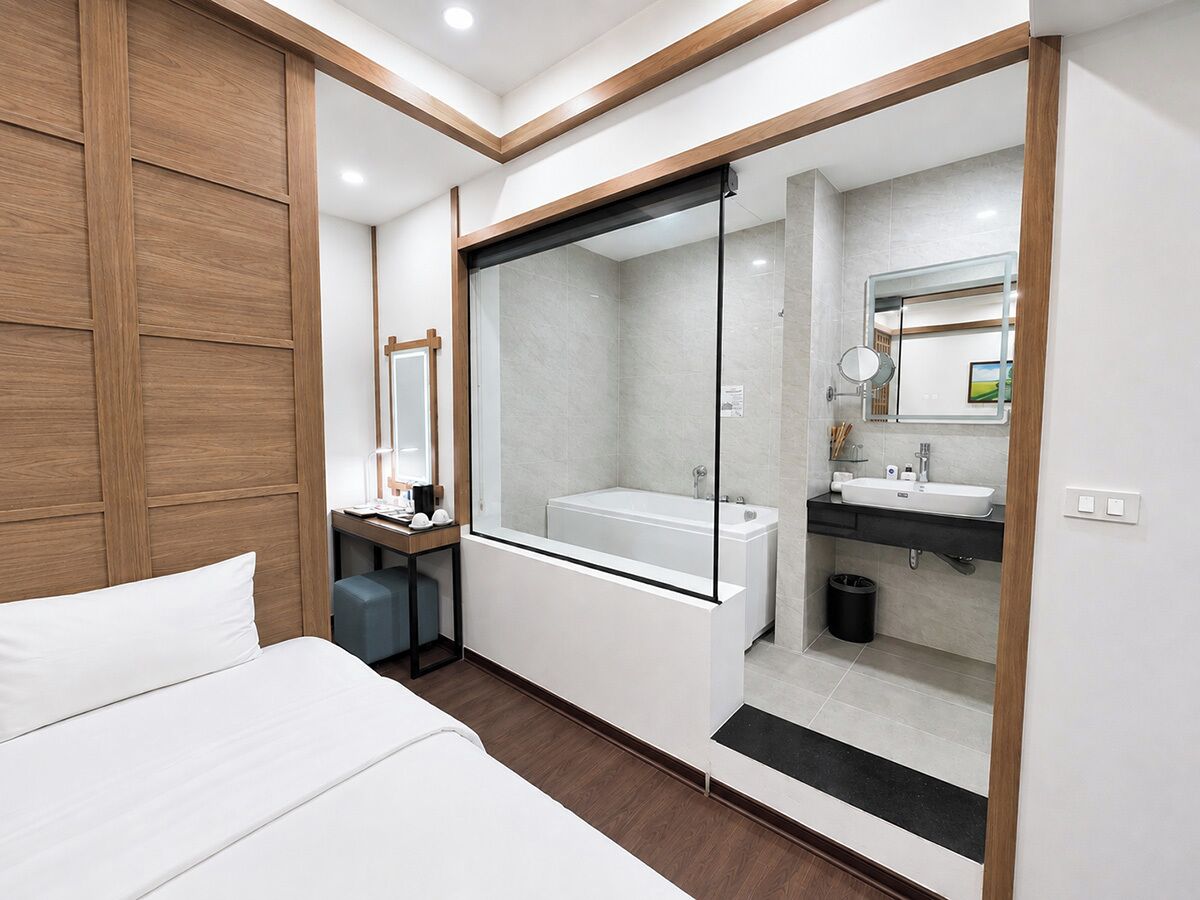 A modern hotel room with a large bed, a walk-in closet, a bathroom with a bathtub, and a vanity with a mirror.