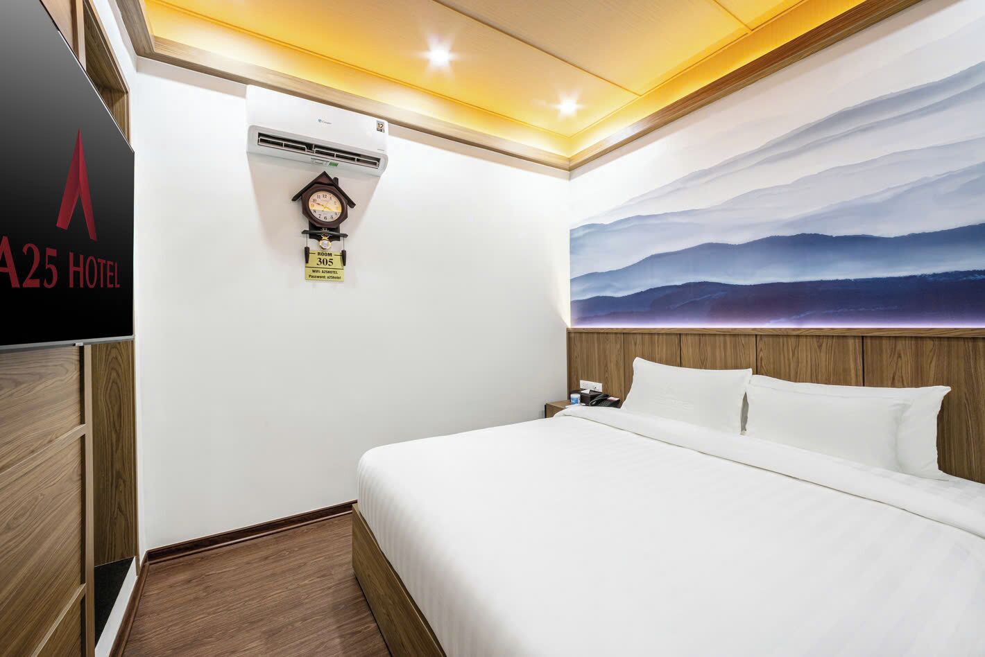 Una habitación de hotel con cama, reloj, equipo de aire acondicionado y un cuadro de un paisaje montañoso.