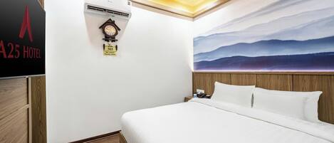 Una habitación de hotel con cama, reloj, equipo de aire acondicionado y un cuadro de un paisaje montañoso.