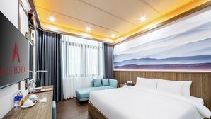 Habitación de hotel con una cama grande, un escritorio con teléfono, una silla y vistas a las montañas a través de la ventana.