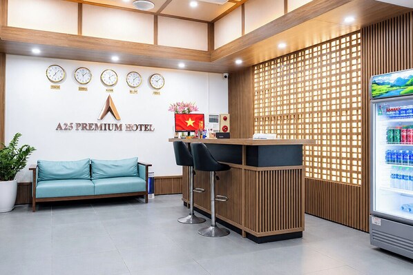 A reception area with a sofa, a reception desk, a wall clock, a flag, and a beverage dispenser. - A25 Premium Hotel - 21 Nghia Tan (Hanoi)