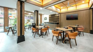 Un moderno vestíbulo de hotel con detalles de madera, un televisor de pantalla plana y un comedor con mesas y sillas.