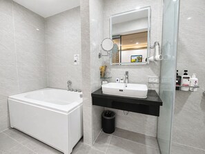 Un baño moderno con una bañera blanca, un tocador con lavamanos negro y un box de ducha de vidrio.