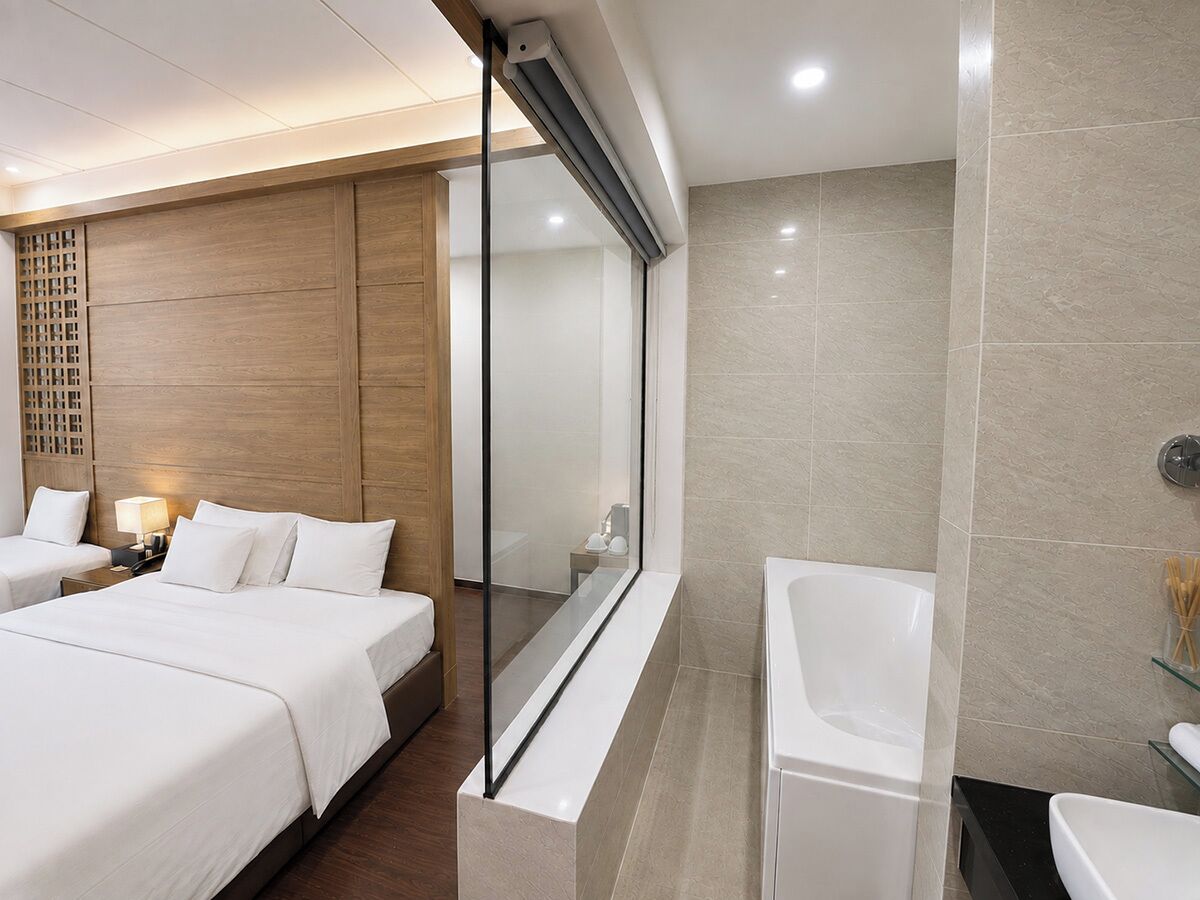 Quarto de hotel com uma cama grande, banheiro separado com banheira e divisória de vidro entre os dois.