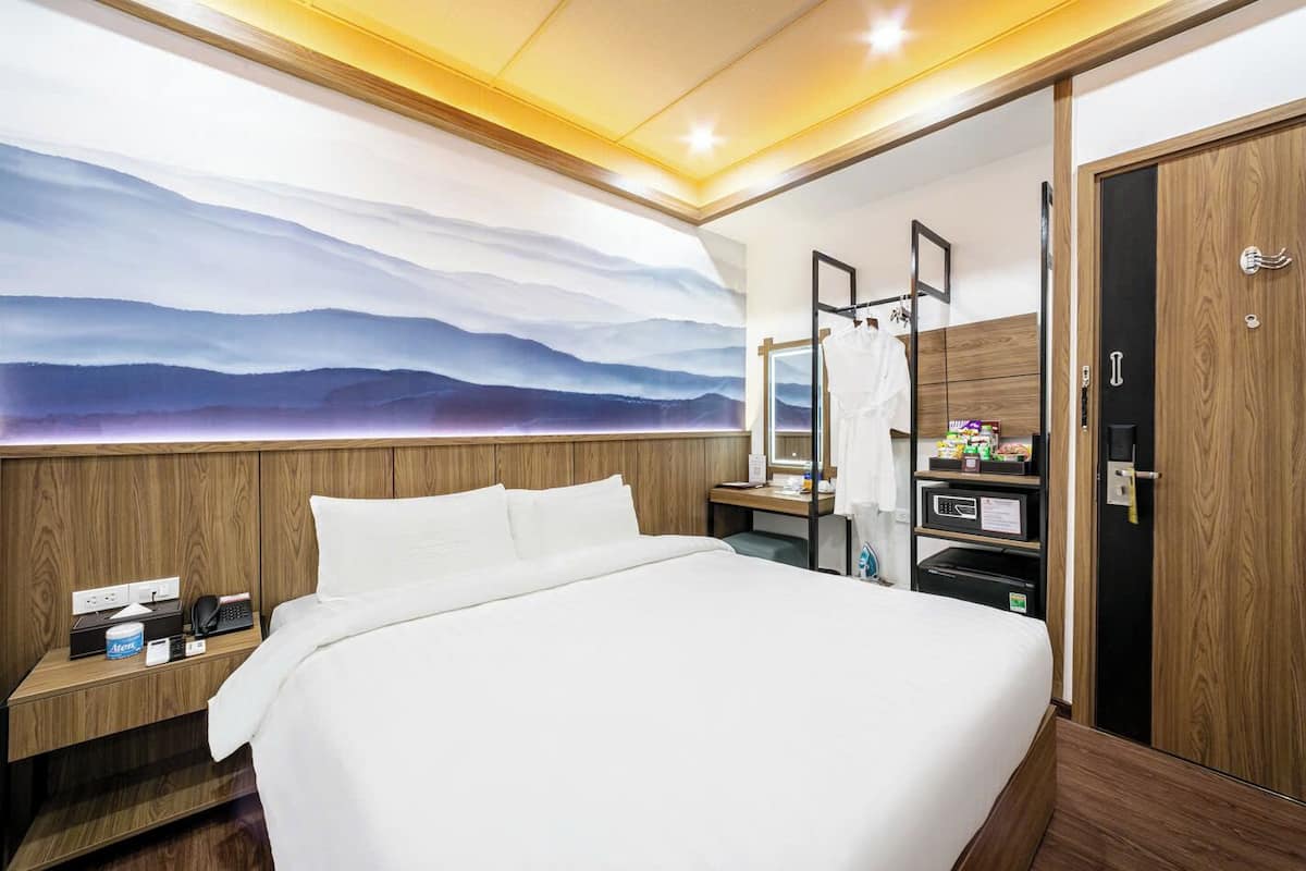 Ein Hotelzimmer mit einem großen Bett, einem Holzkopfteil, einem Nachttisch mit Telefon und Lampe, einem an der Wand montierten Fernseher und einem Holzschrank.