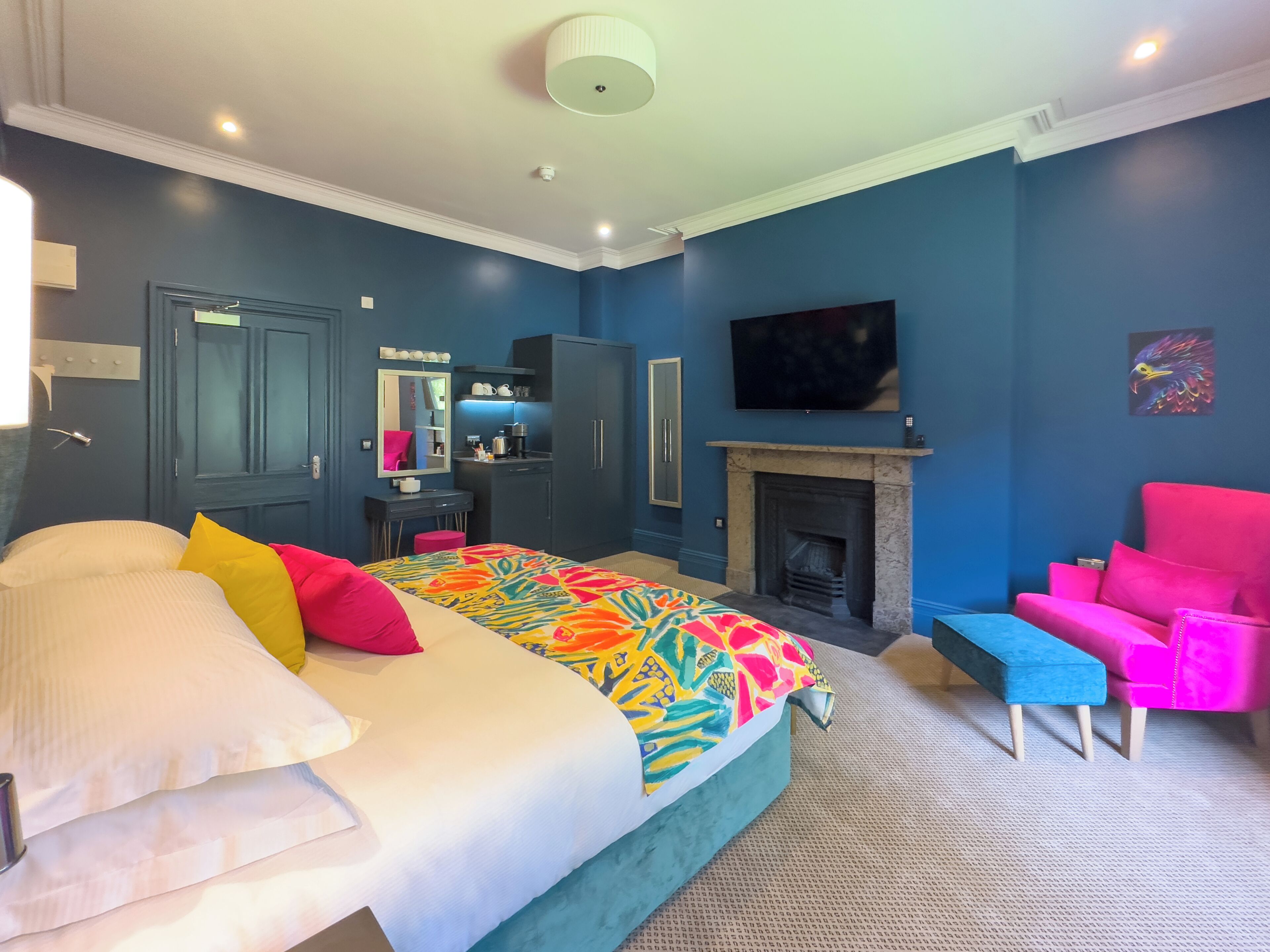 A bedroom with a bed, a desk, a chair, a TV, and a fireplace.