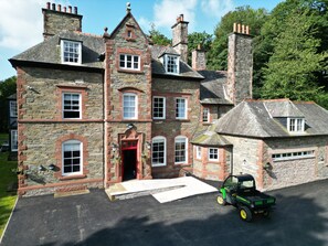 A large stone building with multiple chimneys, a red door, and a green utility vehicle parked in front.