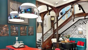 Un salón espacioso con una mesa curva roja, sillas rojas, un sofá color turquesa con cojines rojos y una escalera con barandilla decorativa.