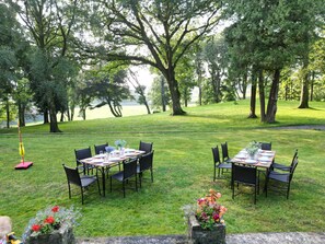 An outdoor dining area with tables and chairs, surrounded by trees and a view of a body of water.