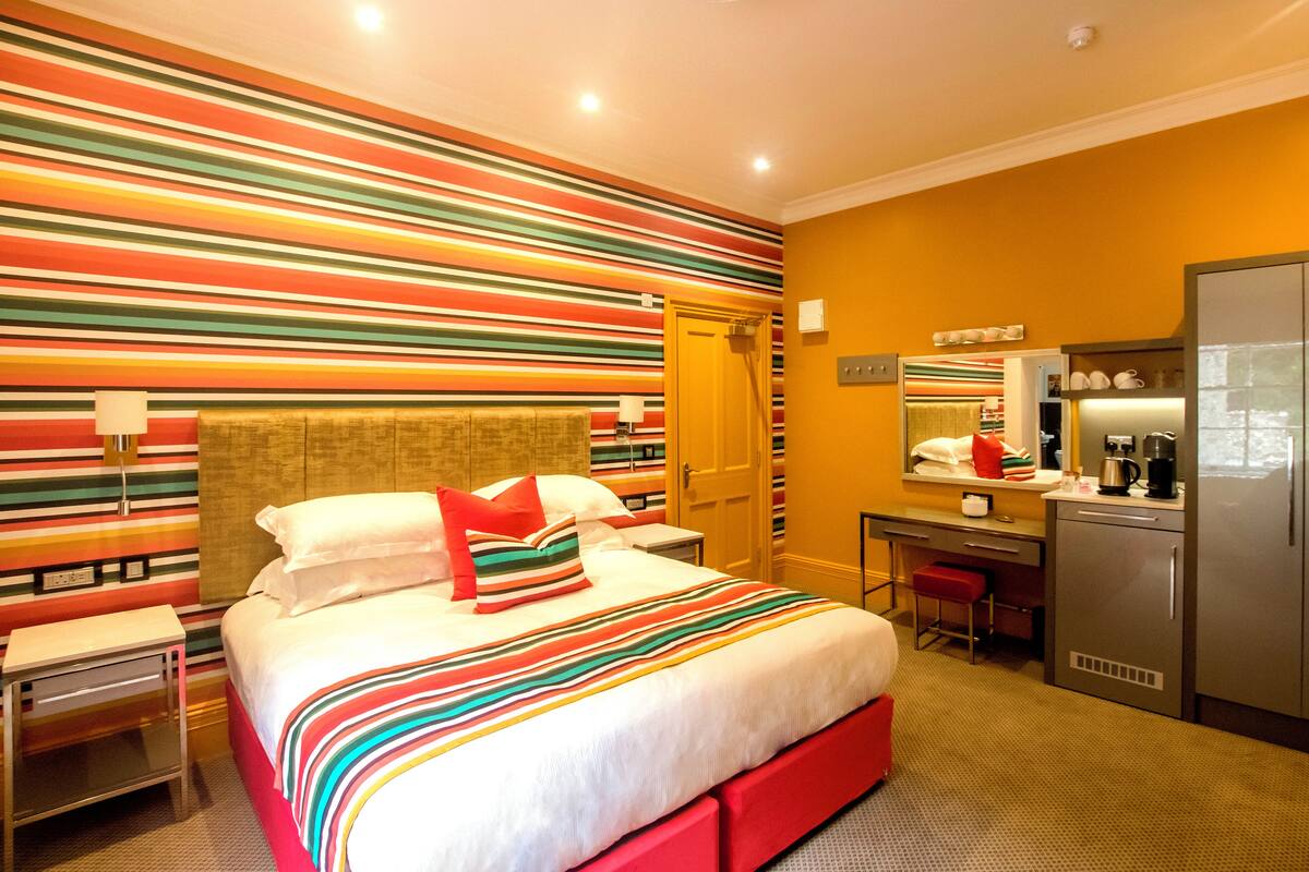 A hotel room with a bed, a desk, a refrigerator, and a striped wall.