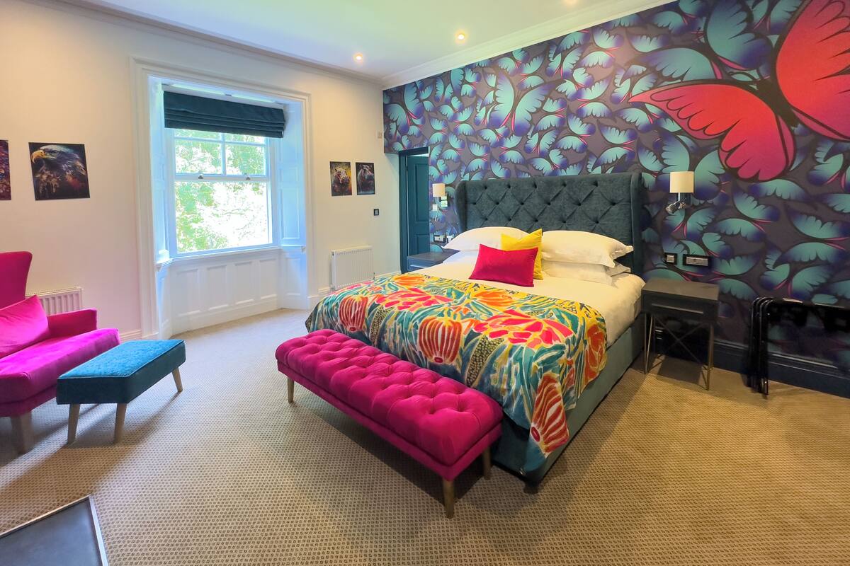 A bedroom with a large bed, a bench, a chair, and a window.