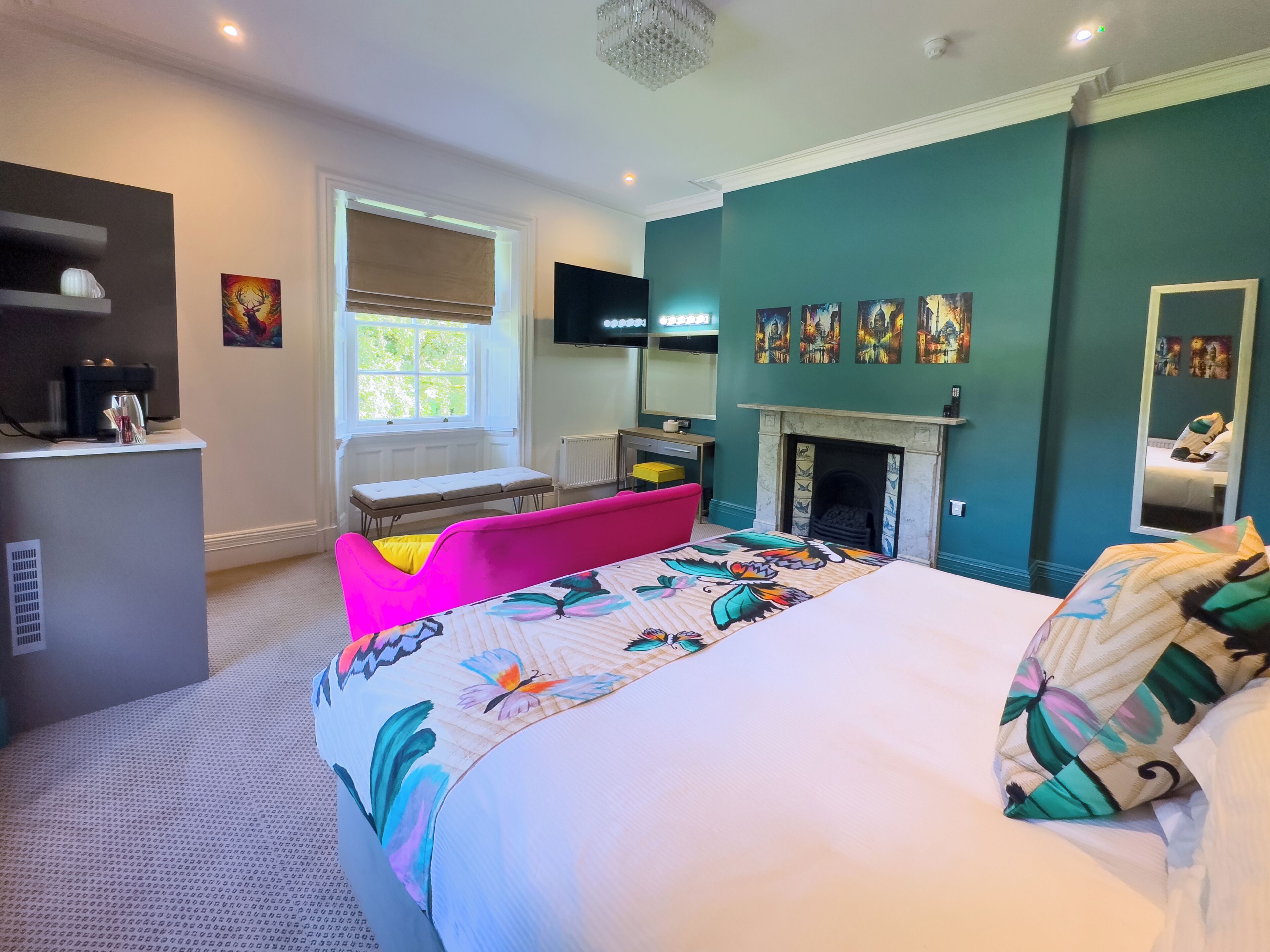 A modern hotel room with a large bed, a pink sofa, a fireplace, and artwork on the walls.