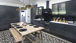Una cocina moderna con armarios oscuros, una mesa de madera con taburetes circulares negros y un suelo con estampado.
