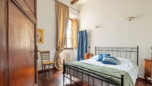 A bedroom with a wooden floor, a metal bed frame, a green bedspread, and a window with curtains. - Cozy and Stylish 2-Bedroom Apartment in Central Rome
 (Roma)