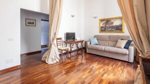 A room with a wooden floor, a sofa, a table, and a chair. - Cozy and Stylish 2-Bedroom Apartment in Central Rome
 (Roma)