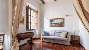 A room with a wooden floor, a sofa, a small table, a lamp, and a painting on the wall. - Cozy and Stylish 2-Bedroom Apartment in Central Rome
 (Roma)