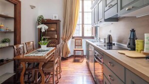 A compact kitchen with wooden cabinets, a dining table with chairs, and a window with curtains. - Cozy and Stylish 2-Bedroom Apartment in Central Rome
 (Roma)
