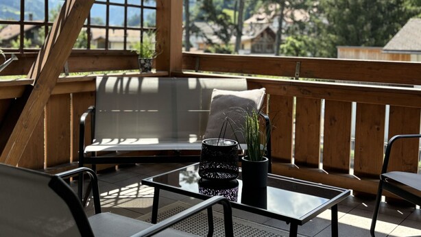 A wooden deck with a glass table, a bench, and a chair. There are potted plants on the table. - Mountain View by Interhome (Frutigen)