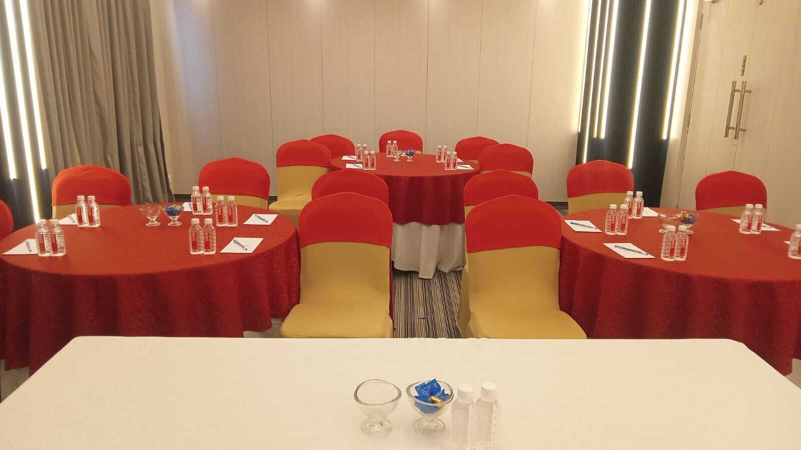 A conference room with multiple tables, each with red tablecloths and yellow chairs. Water bottles and glasses are placed on the tables.