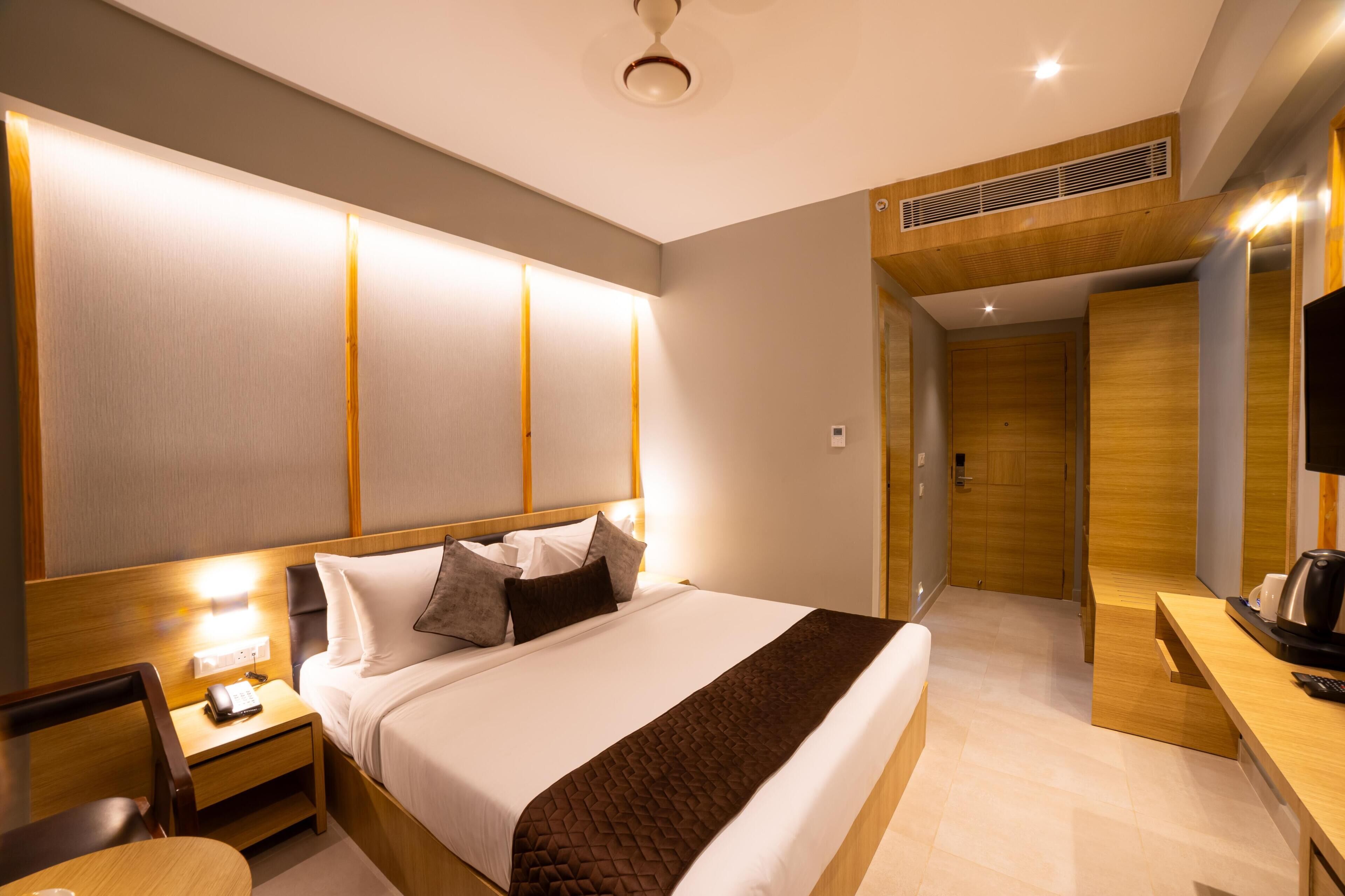 A modern hotel room with a large bed, bedside table, and a desk area with a coffee maker.
