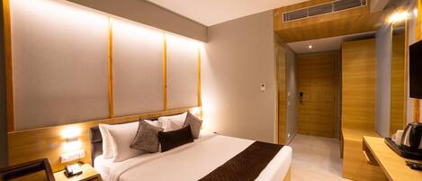 A modern hotel room with a large bed, bedside table, and a desk area with a coffee maker.