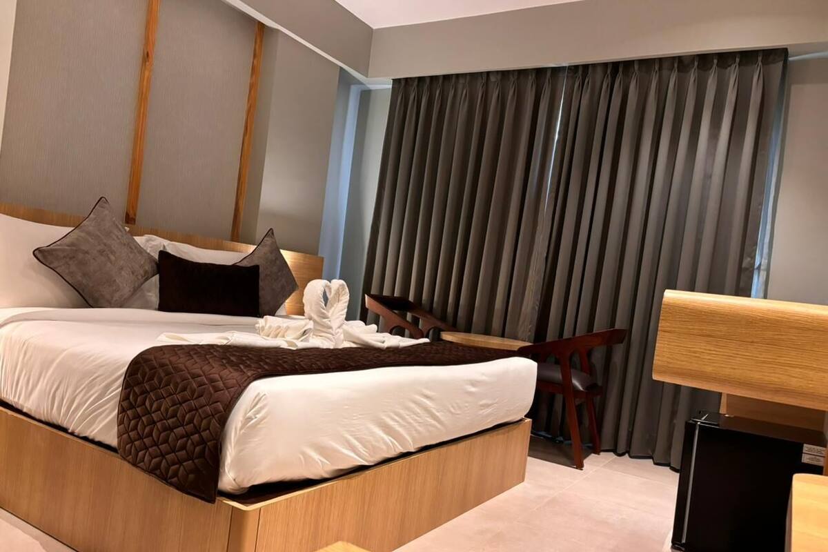 Une chambre d’hôtel moderne avec un grand lit, une tête de lit en bois, un bureau et une chaise.