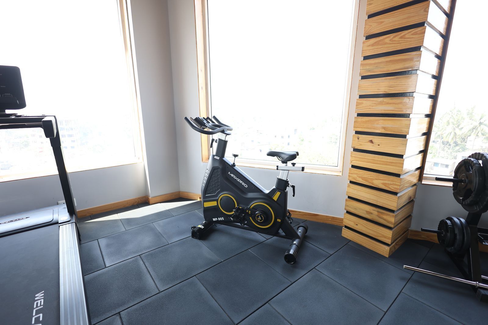 Un gimnasio con una bicicleta estática, un banco de pesas y un ventanal con vistas a edificios.