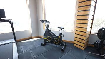Un gimnasio con una bicicleta estática, un banco de pesas y un ventanal con vistas a edificios.
