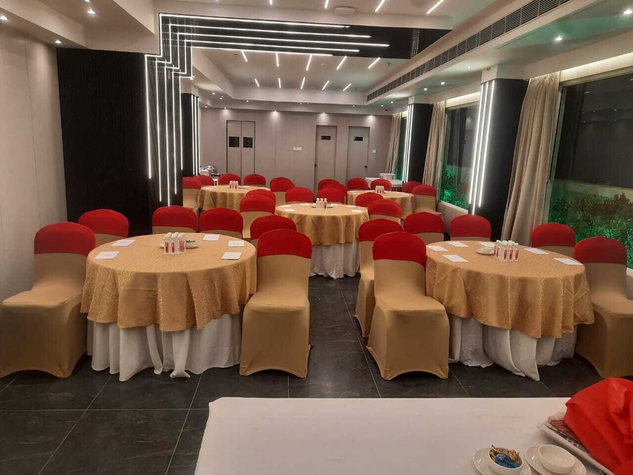 A conference room with multiple round tables, each covered with a beige tablecloth and red chairs.