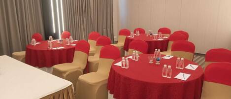 A conference room with multiple round tables, each covered with a red tablecloth and surrounded by beige chairs with red headrests.