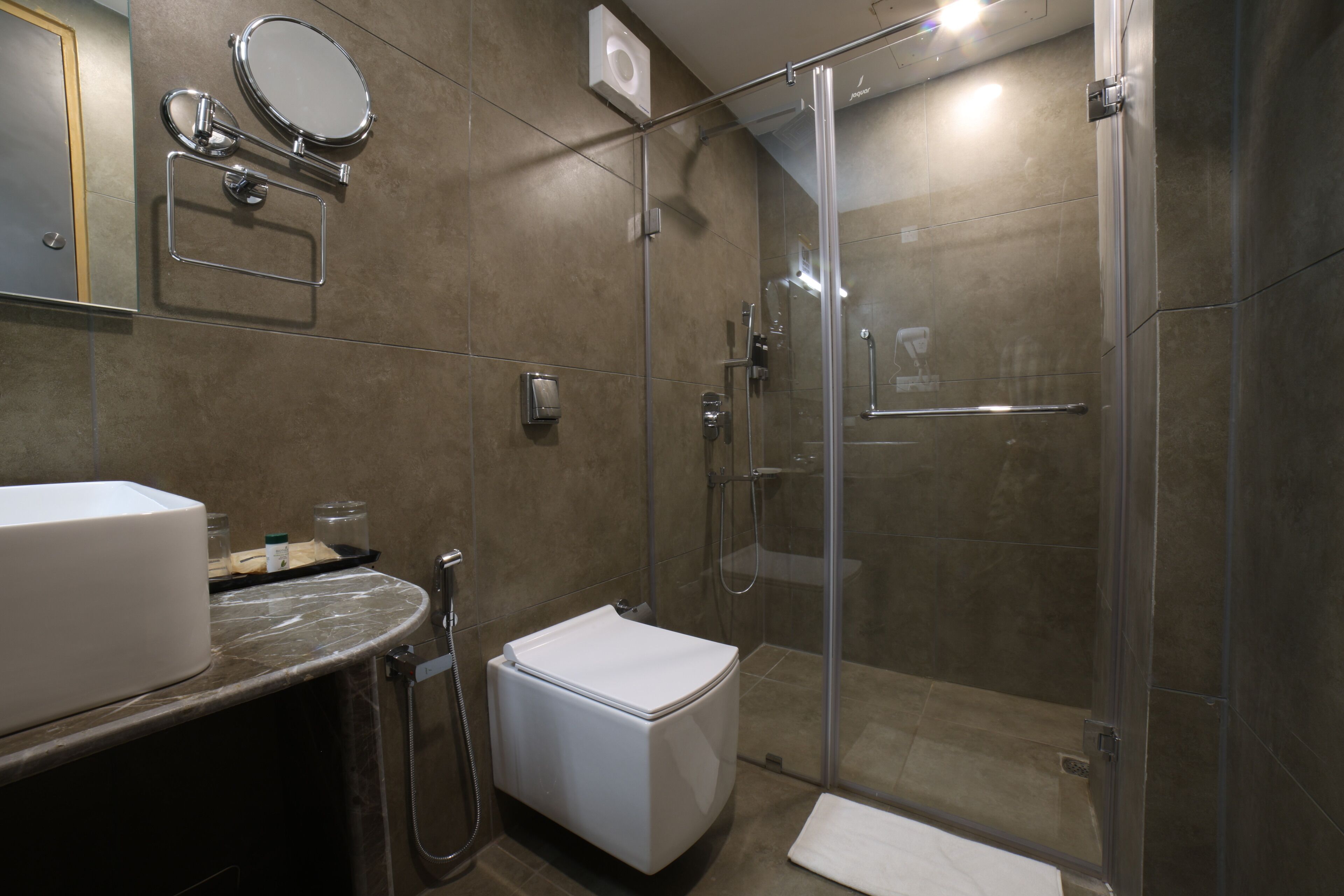 Une salle de bain moderne avec une douche à parois de verre, des toilettes blanches et un comptoir en marbre.