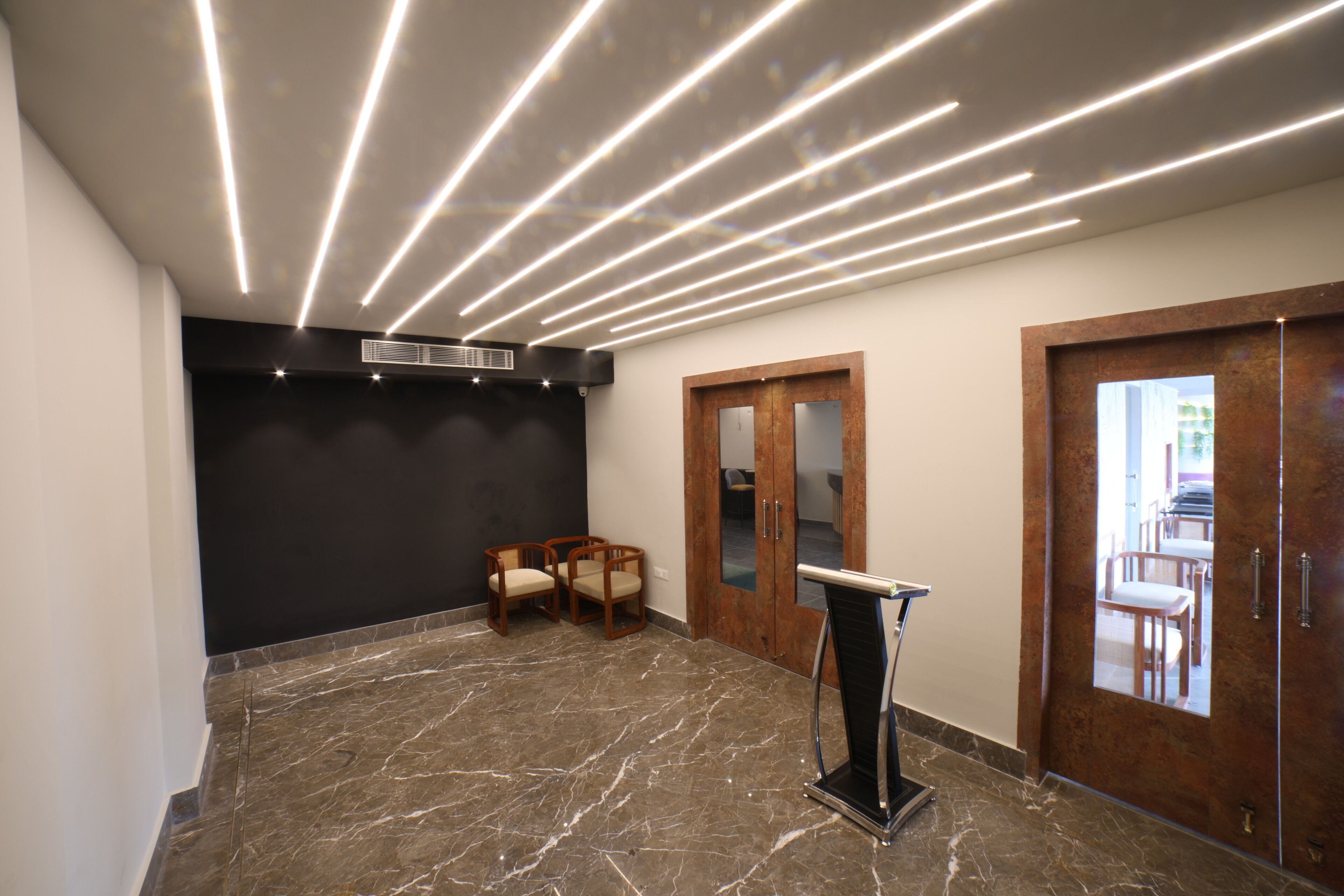 A modern lobby with a marble floor, wooden chairs, a podium, and a black accent wall.